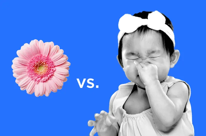 A baby scratching its nose next to a flower.