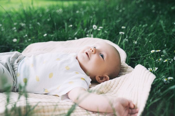 A baby laying on a blanket in the grass.