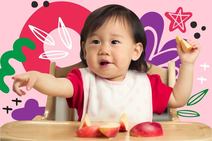 a little girl sitting in a highchair eating a piece of fruit