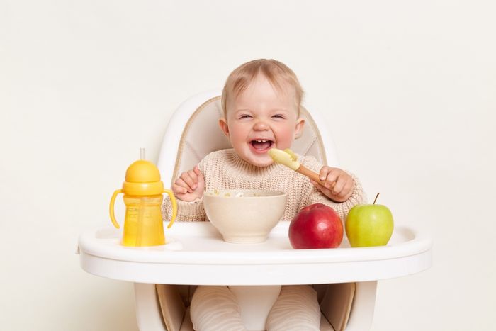 A happy toddler sitting in a chair and eating a meal with formula.