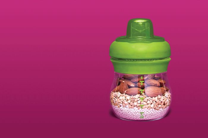 a green sippy cup filled with nuts on a pink background