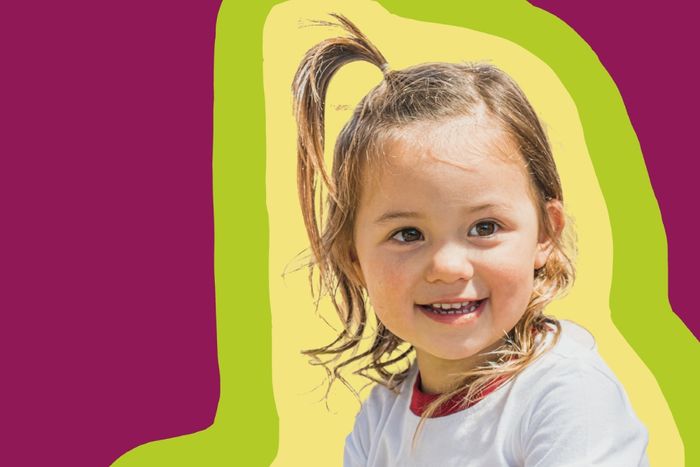 A little girl with a ponytail standing in front of a colorful background.