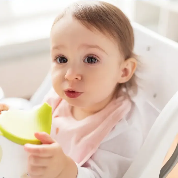 a baby in a highchair eating an apple