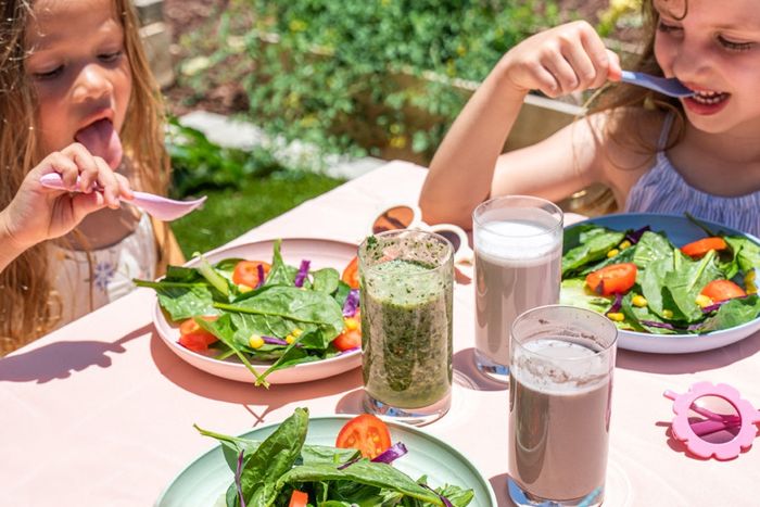 two young girls eating salad at a table