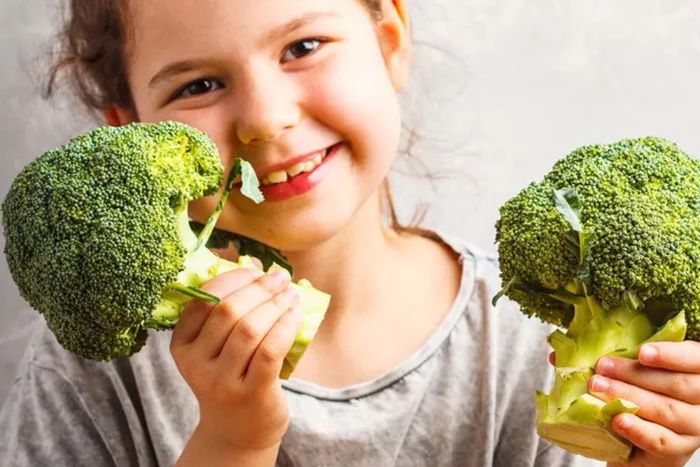 a little girl holding two pieces of broccoli