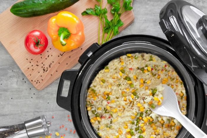 a crock pot filled with rice and vegetables next to a cutting board