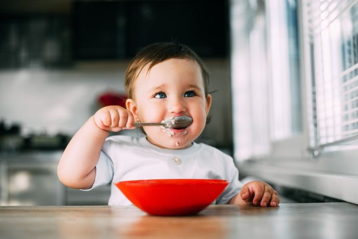 A baby eating food out of a red bowl.