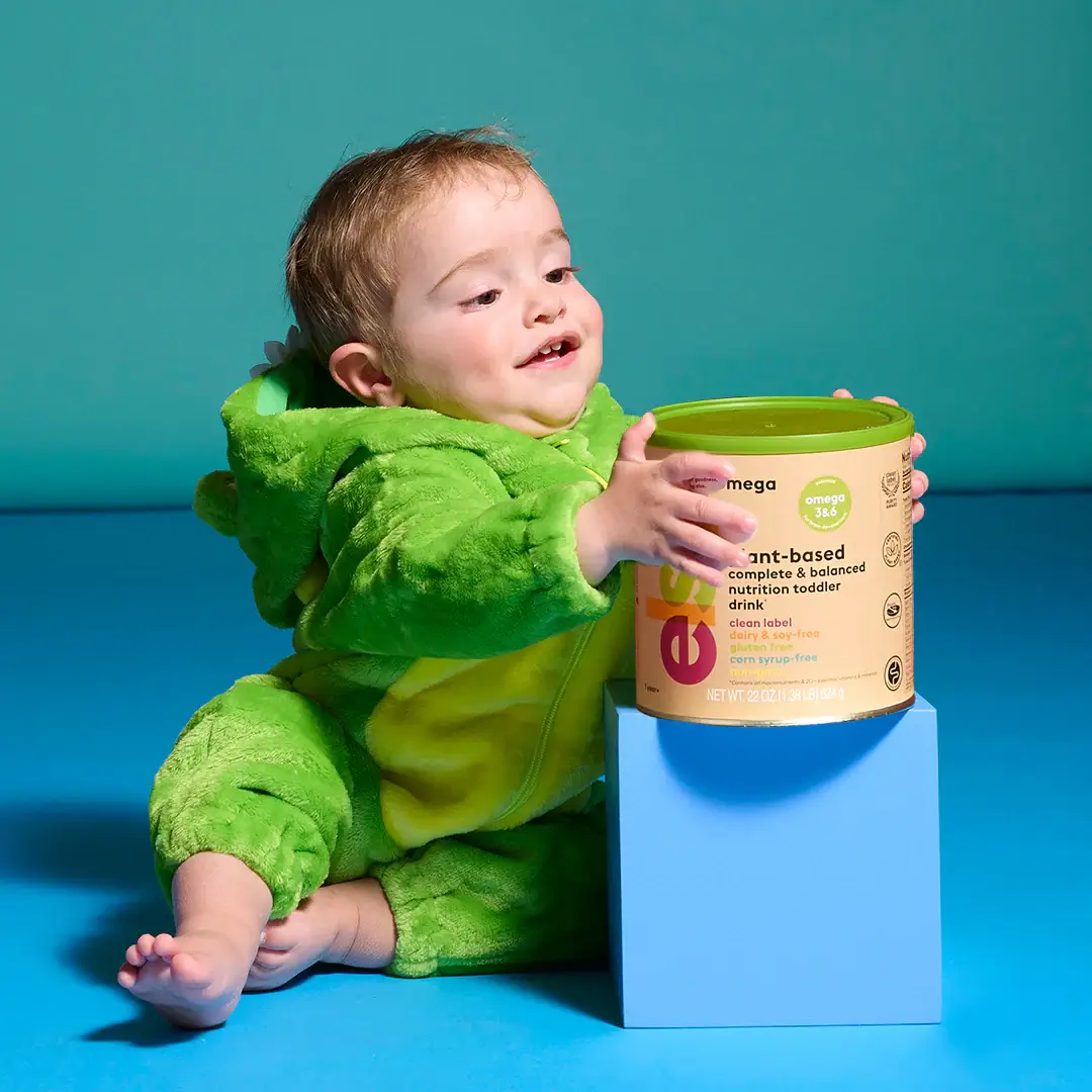 a baby in a green dinosaur costume playing with a can of baby food