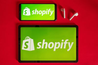 Shopify web page displayed on a modern laptop, smartphone and notebook on red background.