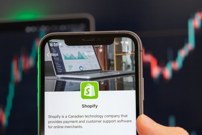 Man holding a mobile phone with shopify company logo.
