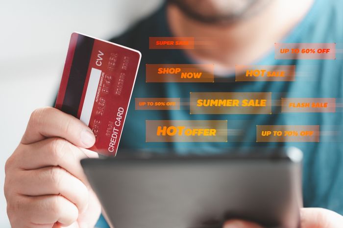 A person holding a credit card and a tablet while browsing seasonal sales online