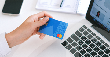 female hand holding a credit card, laptop and notepad in the background