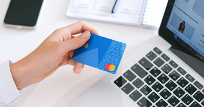 female hand holding a credit card, laptop and notepad in the background