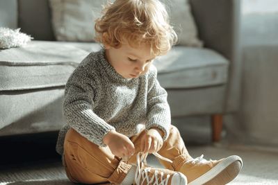 A little boy sitting on the floor trying on hard-bottom shoes.