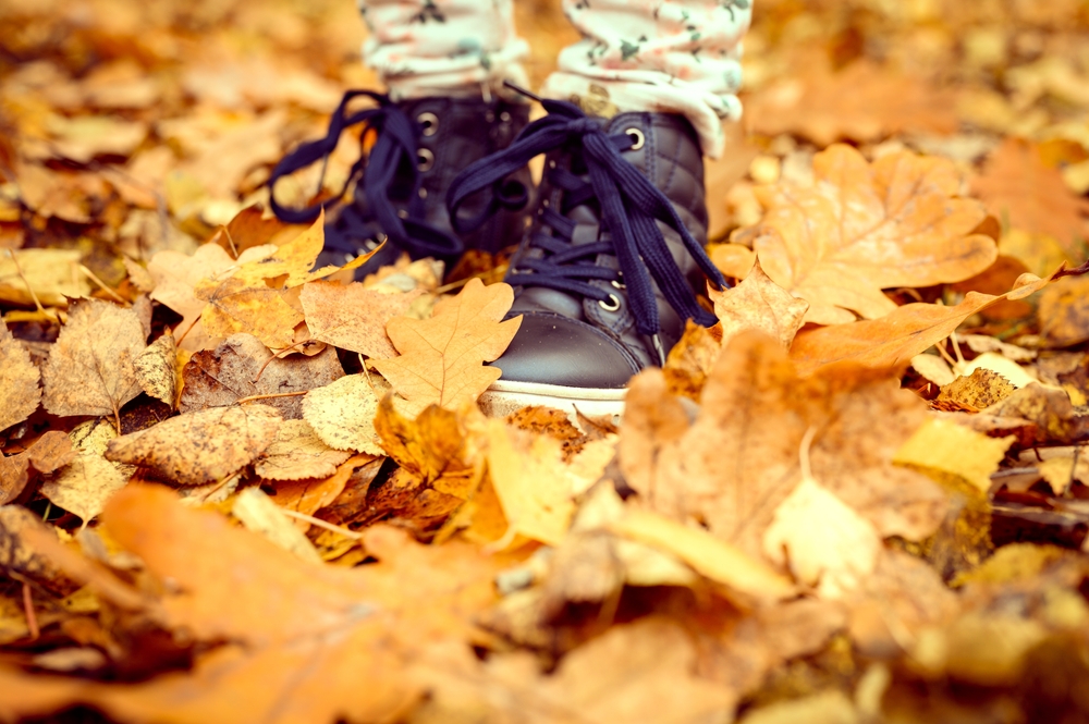 Children's feet in high-top shoes in a pile of autumn fallen orange leaves
