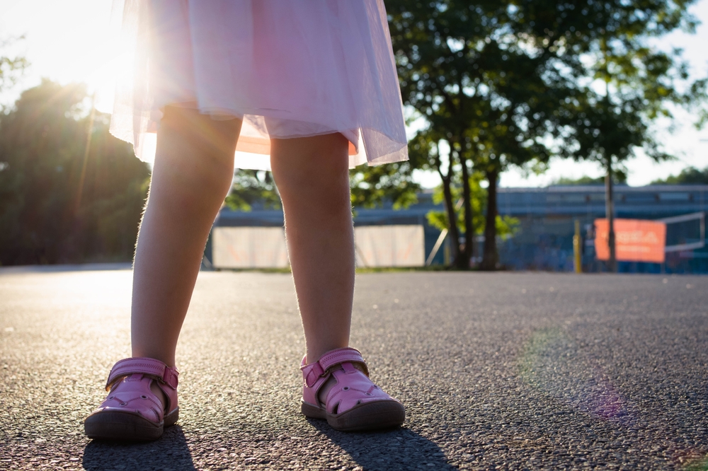 A little girl in pink shoes standing outdoors on a hot day