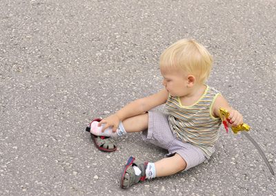 A little boy putting on closed-toe sandals while sitting on the street.