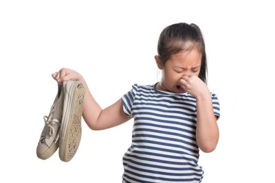 A little girl holding a pair of smelly shoes