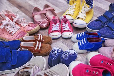 An array of colourful children's school shoes of different styles displayed on a light wooden surface