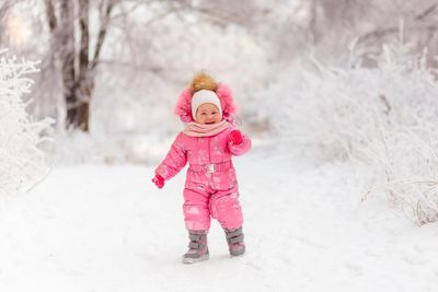 A little girl in a pink snowsuit playing in the snow.