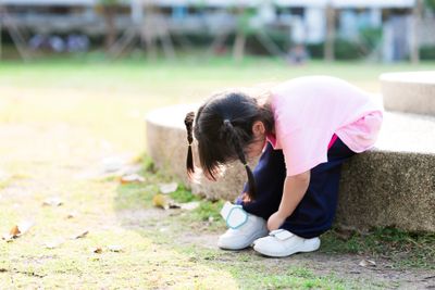 Little girl with tight shoes sitting on a rock and trying to untie them