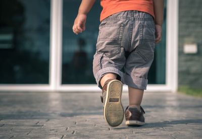 A child walking down a sidewalk with a pair of shoes on to prevent any foot injuries while being outside.