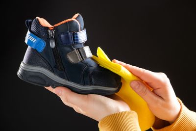 A person wipes a child's shoe on a black background with a yellow rag