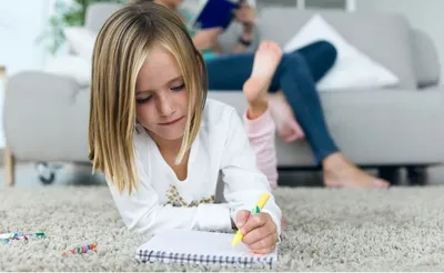 a little girl laying on the floor writing on a piece of paper