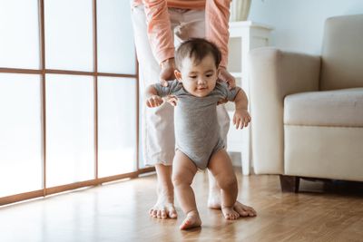 A baby standing on a hard wood floor doing exercises for a waddling gait.