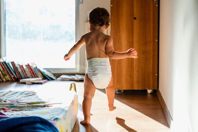 Waddling gait in children: a toddler in a diaper walking next to a bed.
