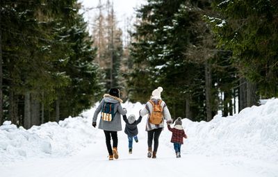 A group of people short-step walking with their children down a snow-covered road