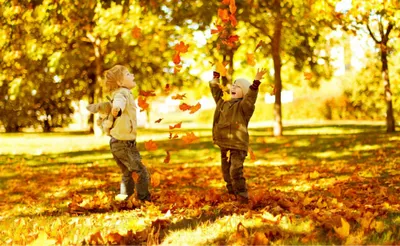 two children playing with leaves in a park