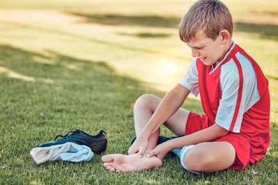 a young boy sitting feeling pain caused by an ill-fitting shoe