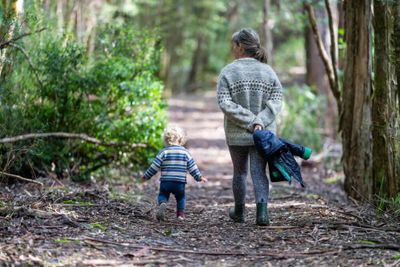 A woman and toddler with hiking boots walking through a forest