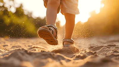 A close up of a child walking on sand.