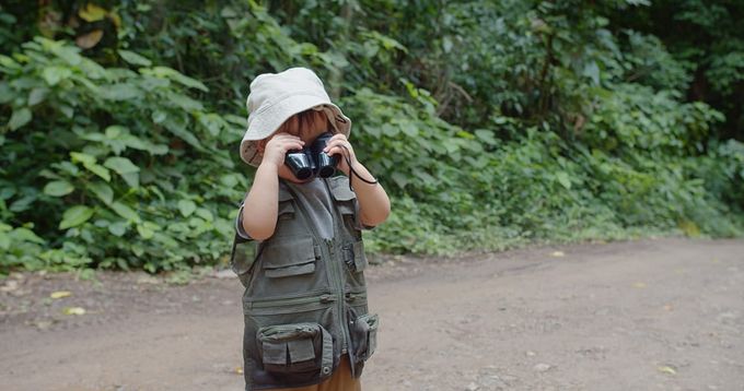 A young boy holding binoculars while hiking on a trail.