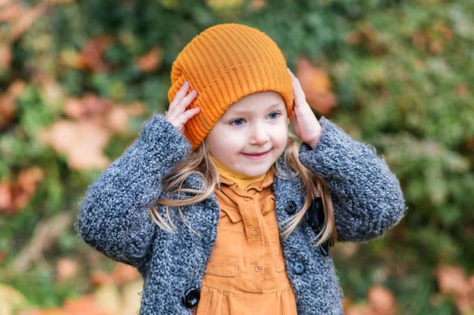 A little girl wearing a knitted orange hat.