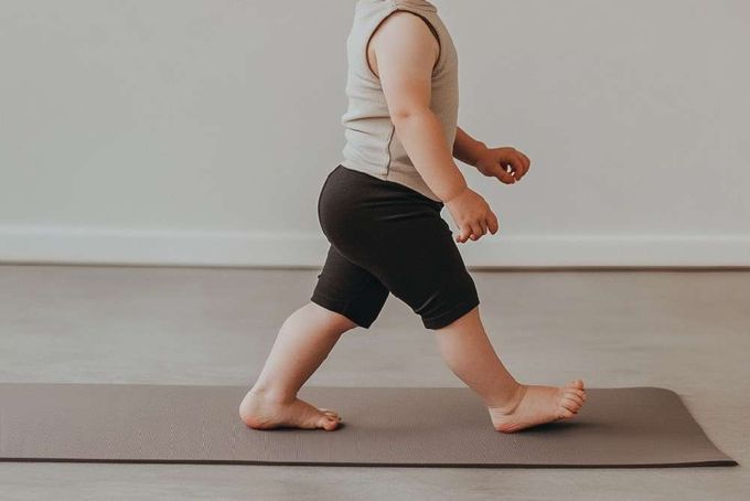 A kid walking on heels on a yoga mat.