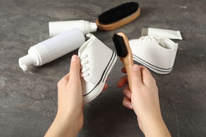 A person holding a brush and cleaning white baby shoes.