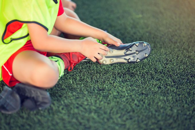 Kid soccer player is sitting holding soles of the foot because of bunions.
