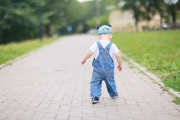 a little boy walking down a sidewalk wearing overalls