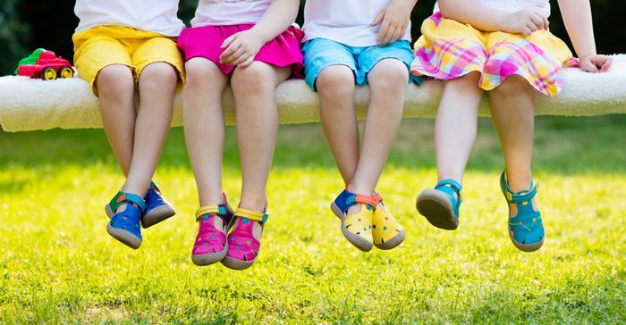 Four preschool children sitting on a tall bench, wearing ankle-supporting footwear.