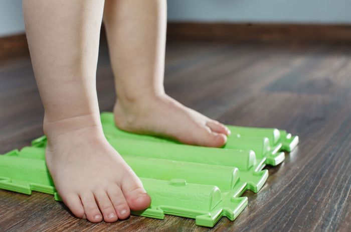 A child standing on a green massage mat to help with his foot pain in the ball or heel .