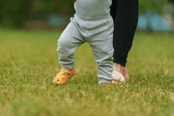 A baby learning to walk while wearing sandals.