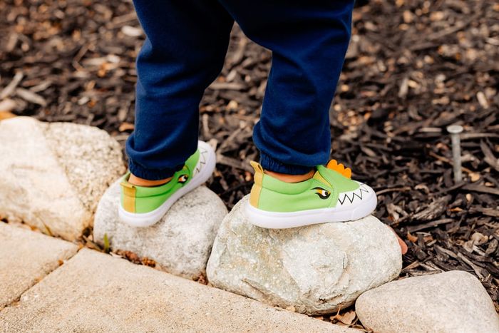Child wearing green dinosaur kids' shoes.