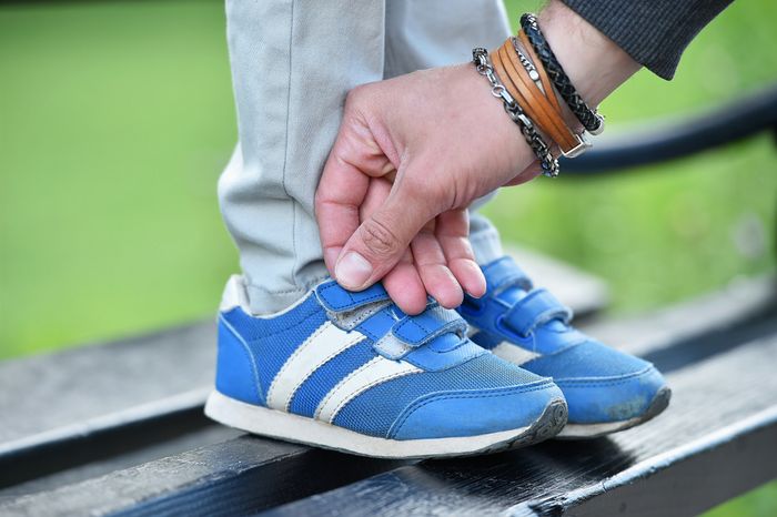A pair of blue Velcro shoes being secured by the parent to child's feet