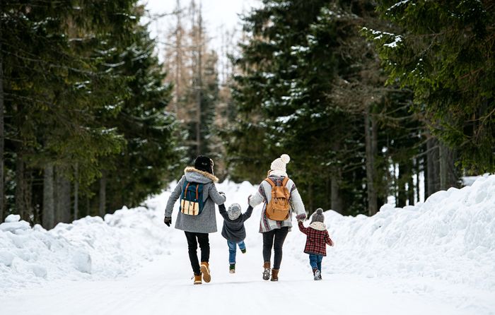 A group of people short-step walking with their children down a snow-covered road