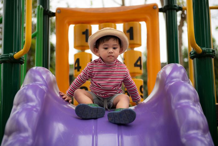 An 18 month old little boy sitting on a purple slide.