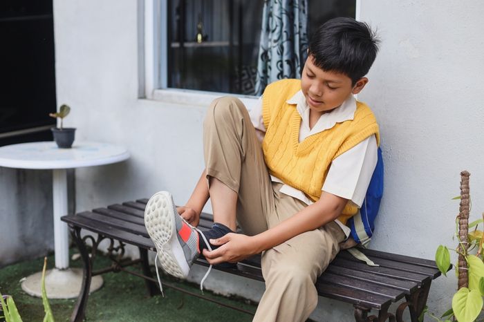 How to label school shoes: a boy sitting on a bench putting on shoes.