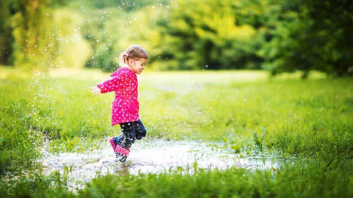 A little girl jumping in a water puddle in a field.